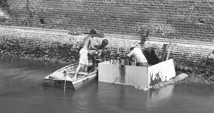 Men in boat repairing moat masonry of Fort