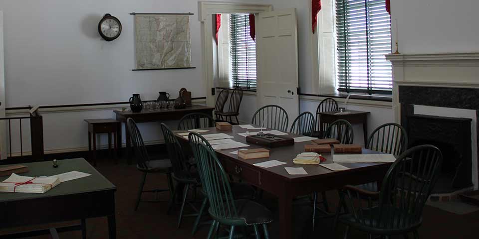 Committee room from the 1700s with Windsor chairs surrounding a wooden table in the center of the room.