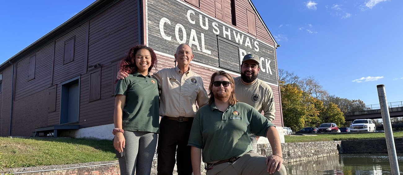 Four volunteers pose for a photo on a dock in front of a red wooden building