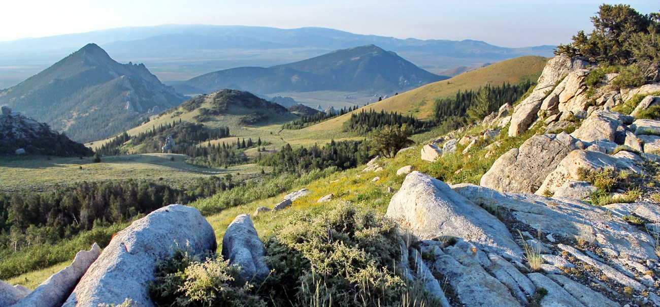 A panoramic view of light-colored rocks, green slopes, and pointed peaks.