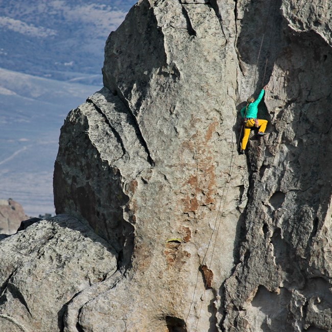 A climber dressed in bright colors ascends a granite formation, beneath a blue sky.