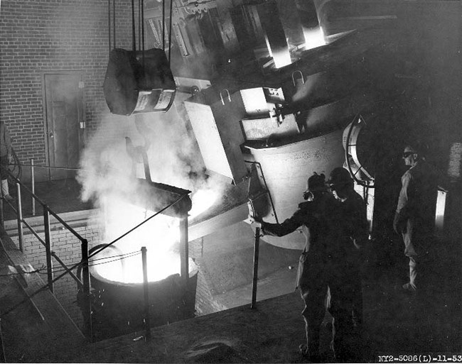 Workers in the foundry wearing protective gear and operating a large machine.