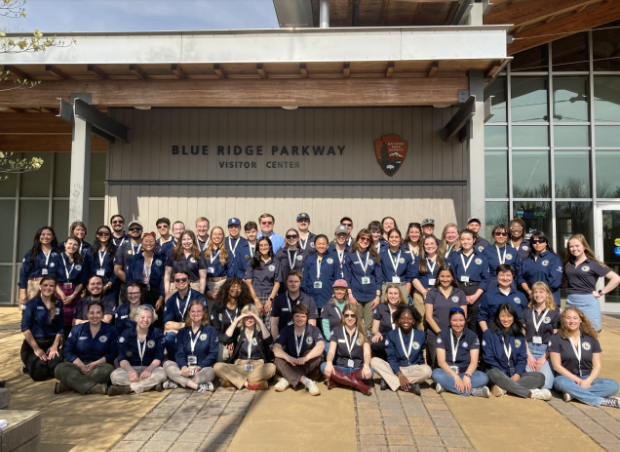 Group poses for a photo in front of the Blue Ridge Parkway Visitor Center building. They are wearing the Community Volunteer Ambassador polo with the official logo displayed on the front