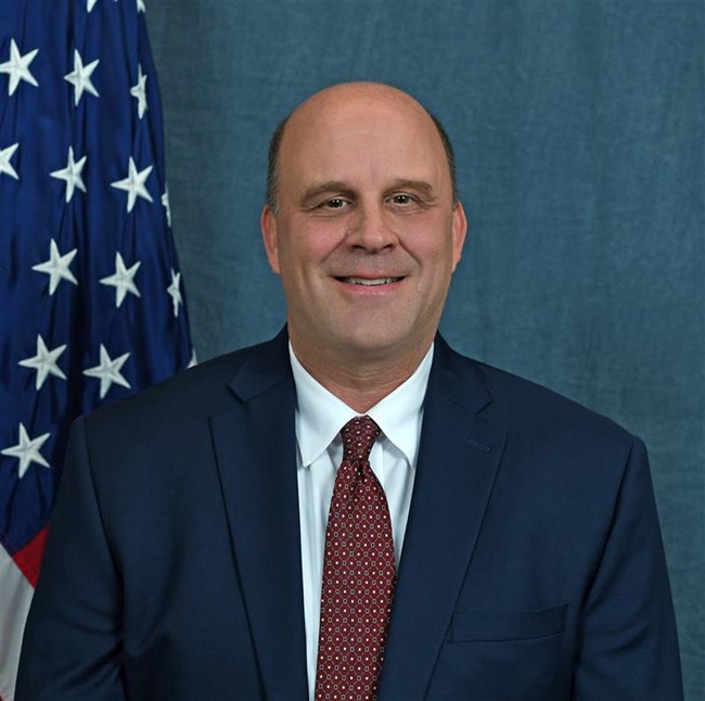 Headshot of a smiling man in front of a blue backdrop