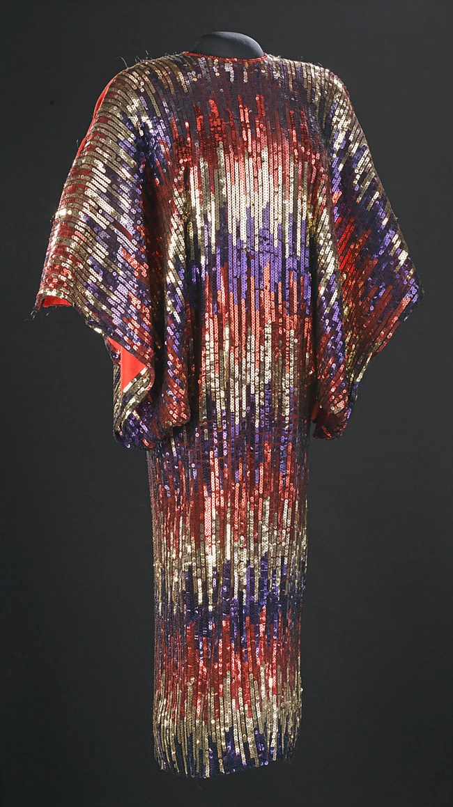 Red, gold, and blue sequin dress designed with horizontal, varied stripes and large open sleeves.