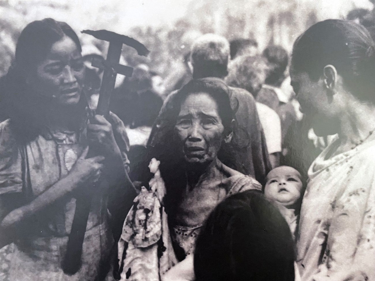 Black and white photo of two women holding religious items flanking distressed older woman in crowd