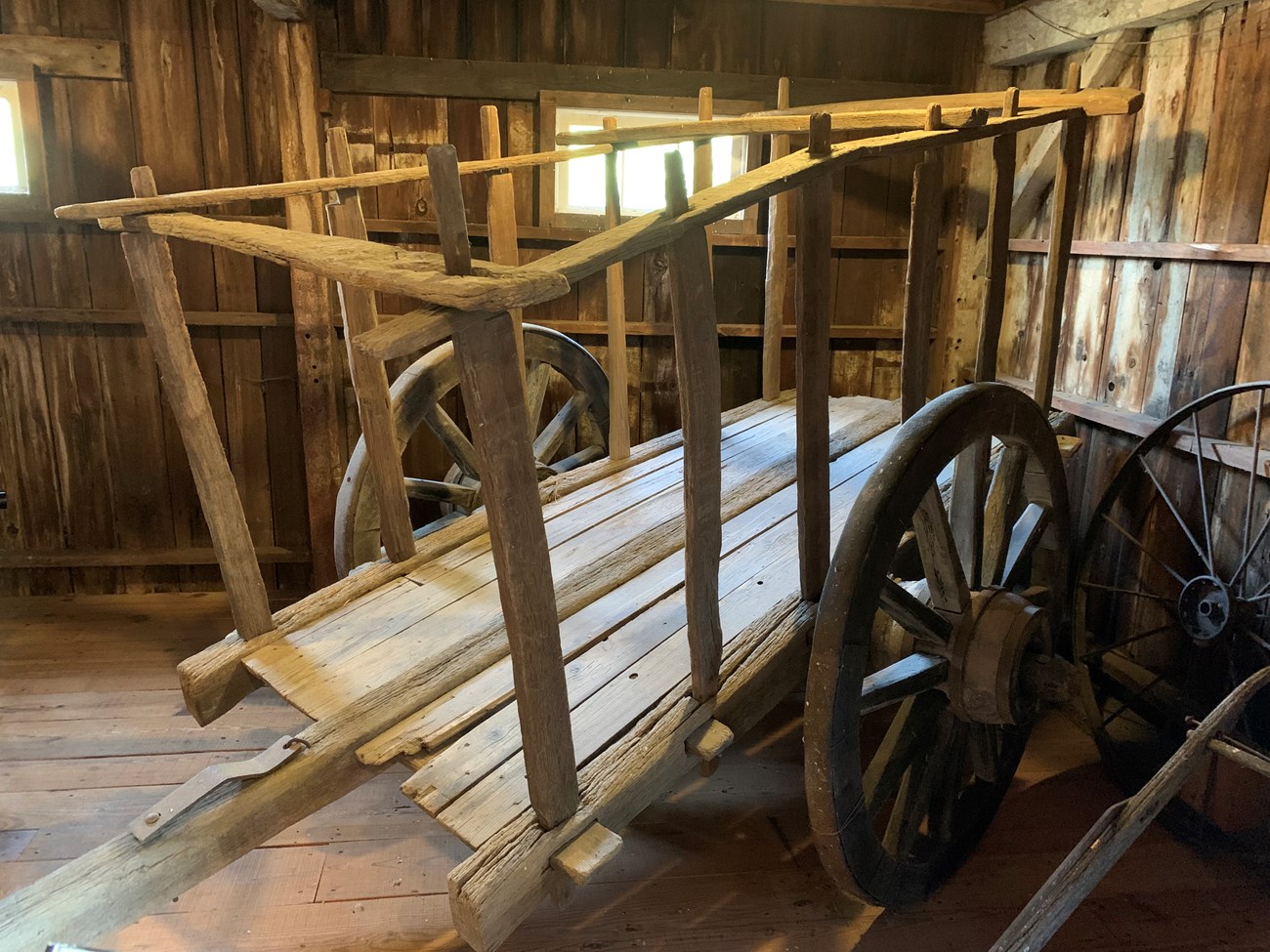 Square wagon made of wood with two wheels inside a wooden horse stable.