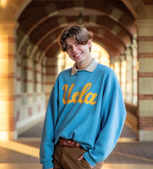 Herman posing under an arch with a blue sweater and brown pants