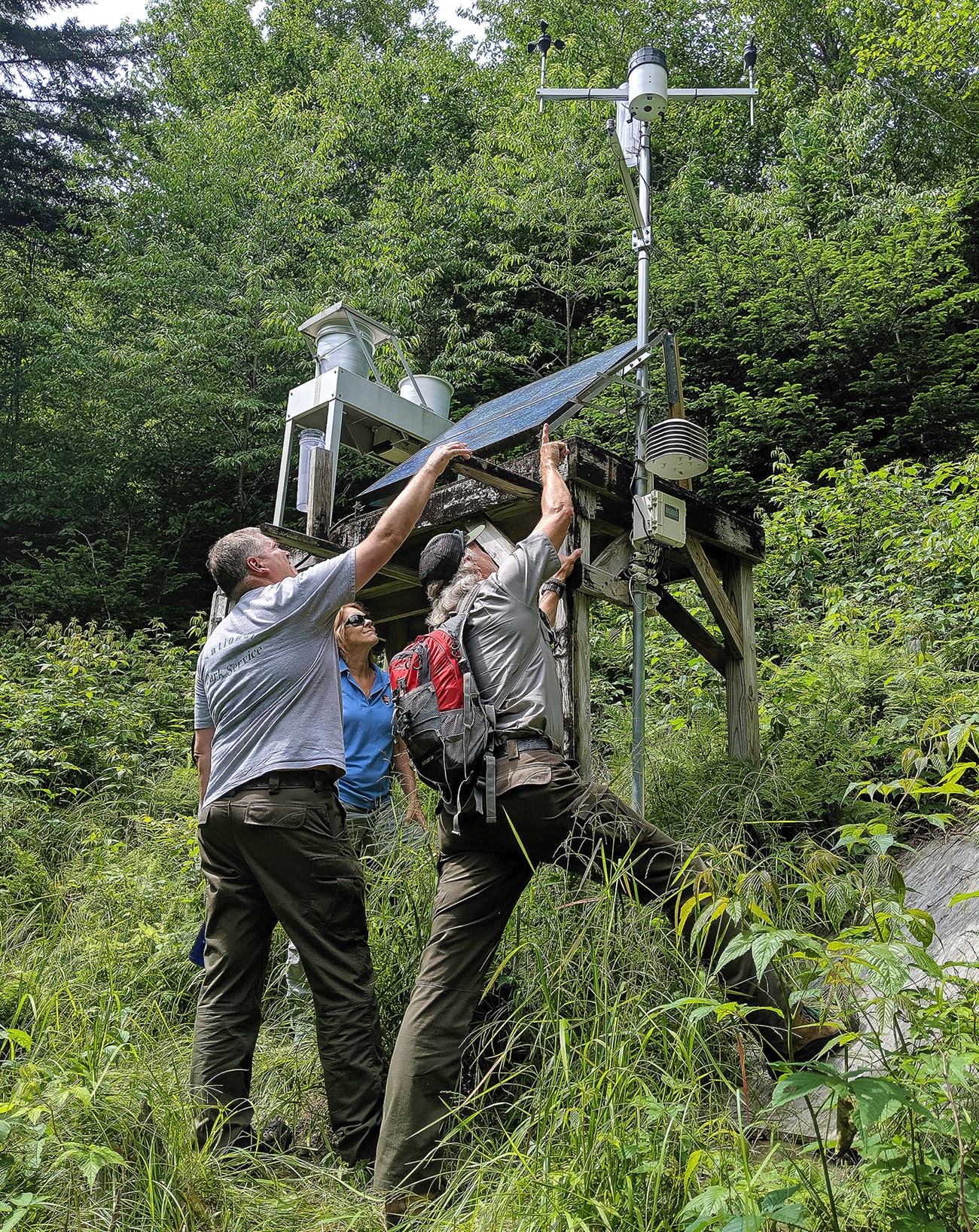 three people check air quality monitoring equipment in a forest
