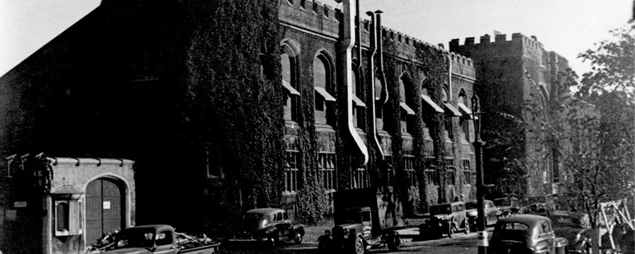 Black and white photo of a gothic-style university building with several cars on the street at the front.