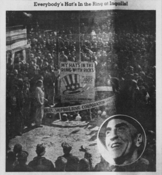 Newspaper photograph of a large crowd with an uncle sam hat on a poster in the middle. A white man's face is in a circle in the bottom right corner