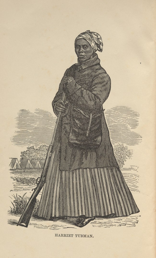 Tubman in traveling clothes standing and holding onto a rifle.