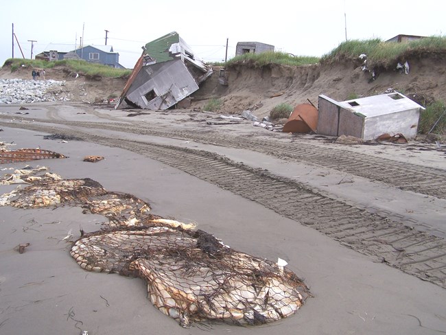 Homes that have fallen off the bluff onto a beach with trash on it.