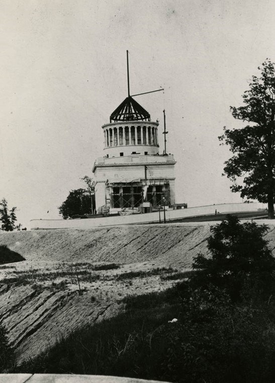 Black and white photo of a white tomb being constructed on top of a raised hill with a blank white background