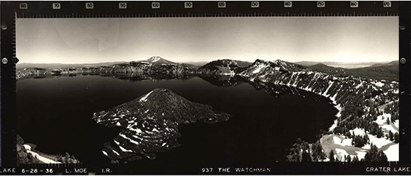 Black and white photo of a massive lake surrounded by trees and mountains.