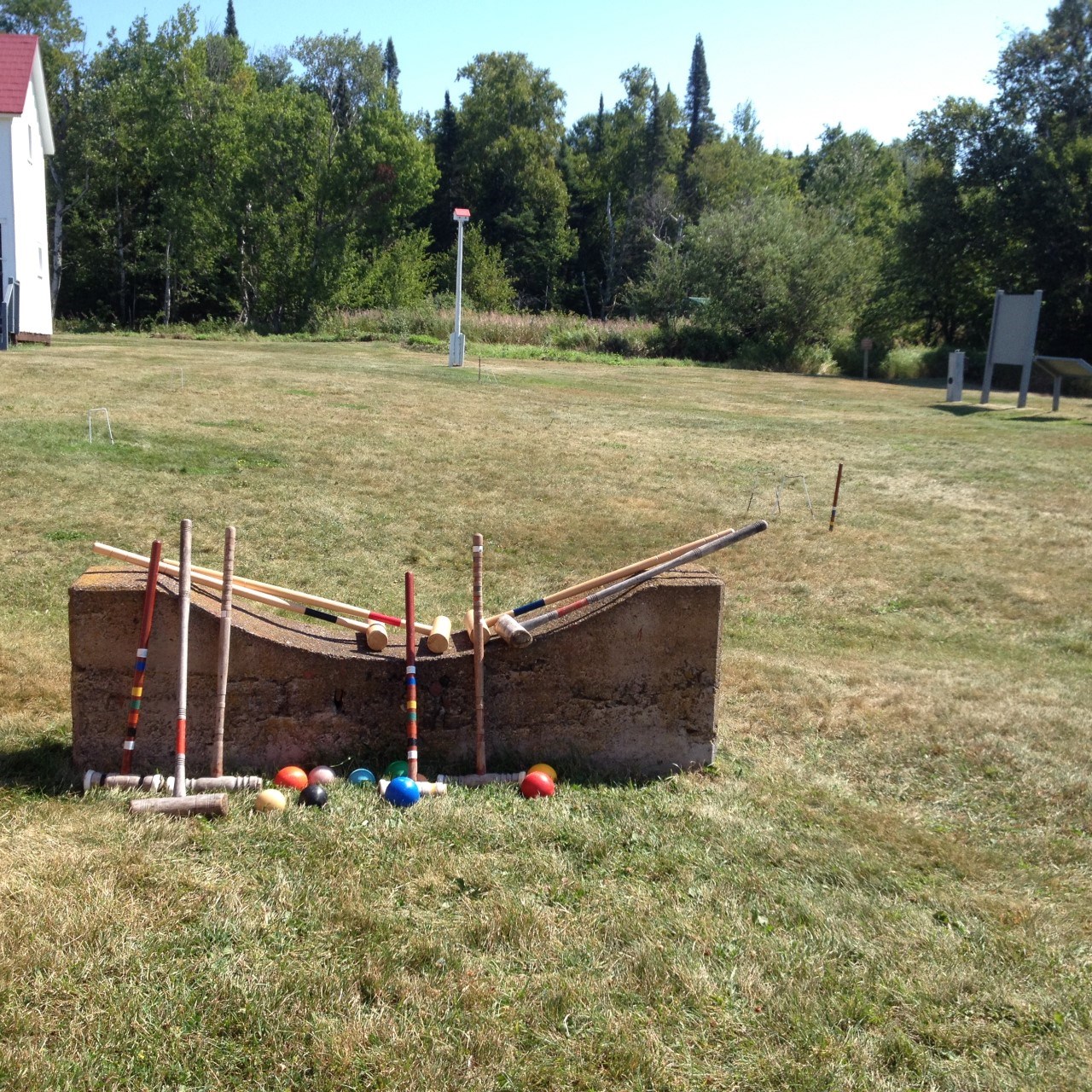 6 wooden croquet mallets propped up on a cement block with different color balls on a green lawn.