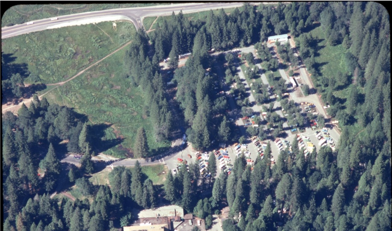 An aerial photograph of a parking lot intermixed with trees.