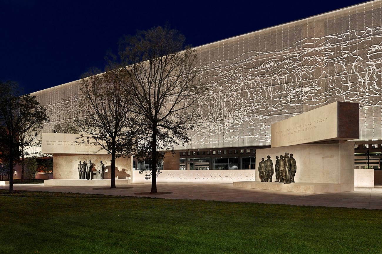 A large metal tapestry hanging over memorial statues of Eisenhower at night