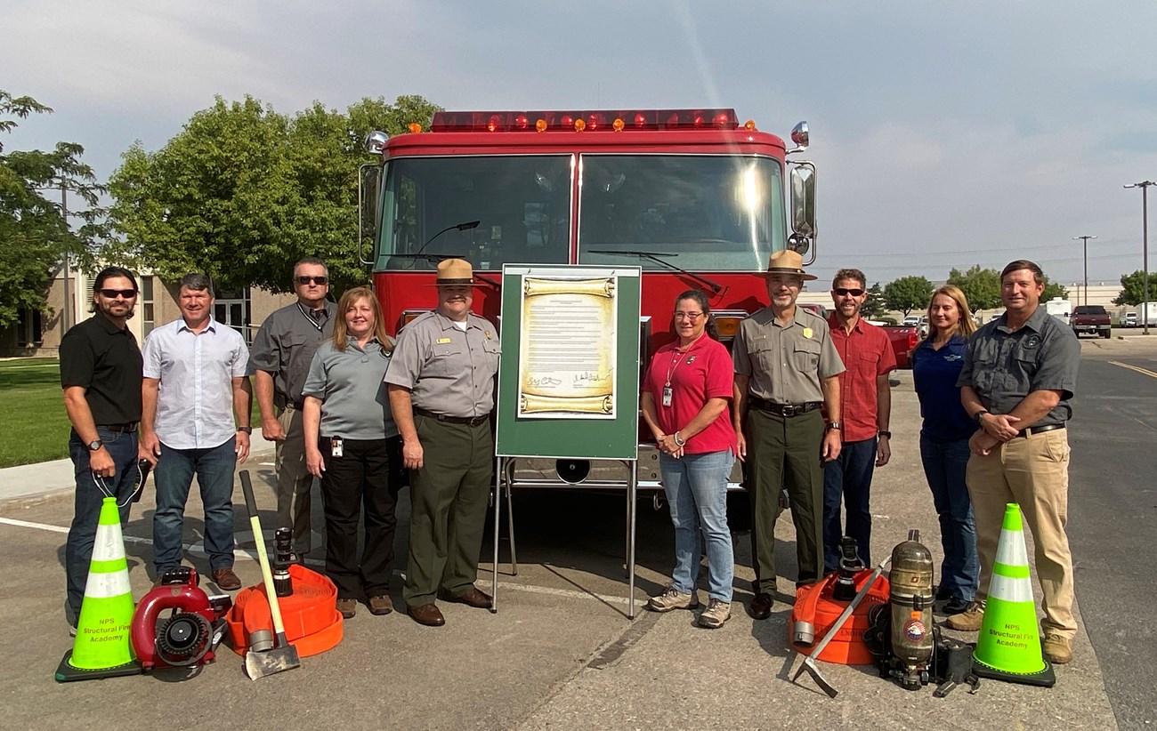 A group of people stand in front of a fire engine with a board holding a sign.