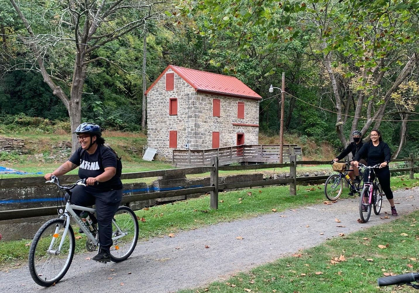 Three bicyclists on bike trail with old stone building with red trim in background