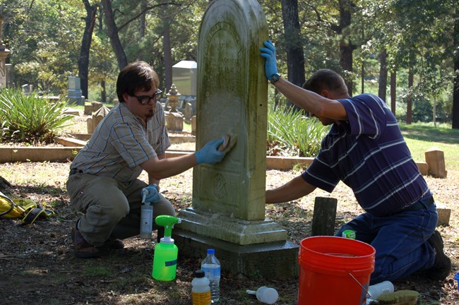Jason Church (left) and a volunteer clean a grave marker.