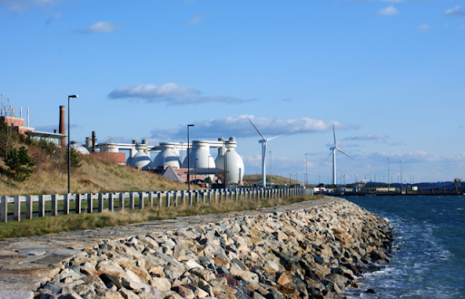 Photo of rocky shore that reaches back towards egg like structures that make up the Deer Island Waste Water Treatment Plant