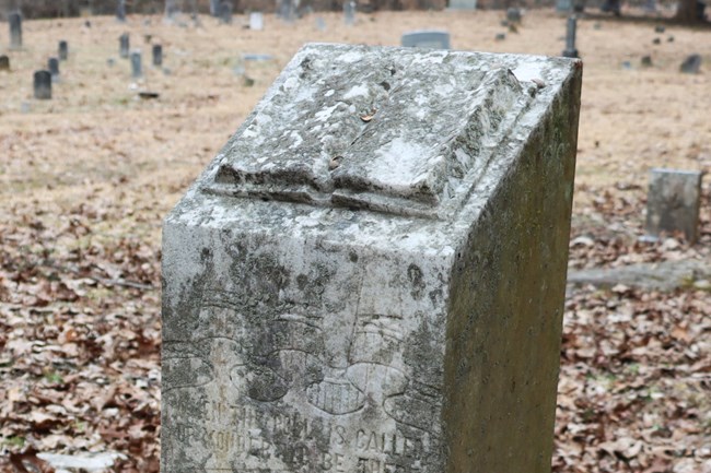 A tombstone with a book and shroud carved into it.