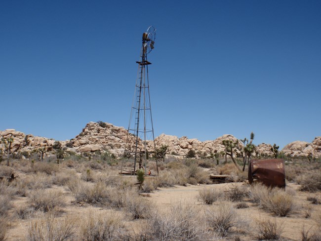 A windmill and a rusty barrel surrounded by a desert landscape