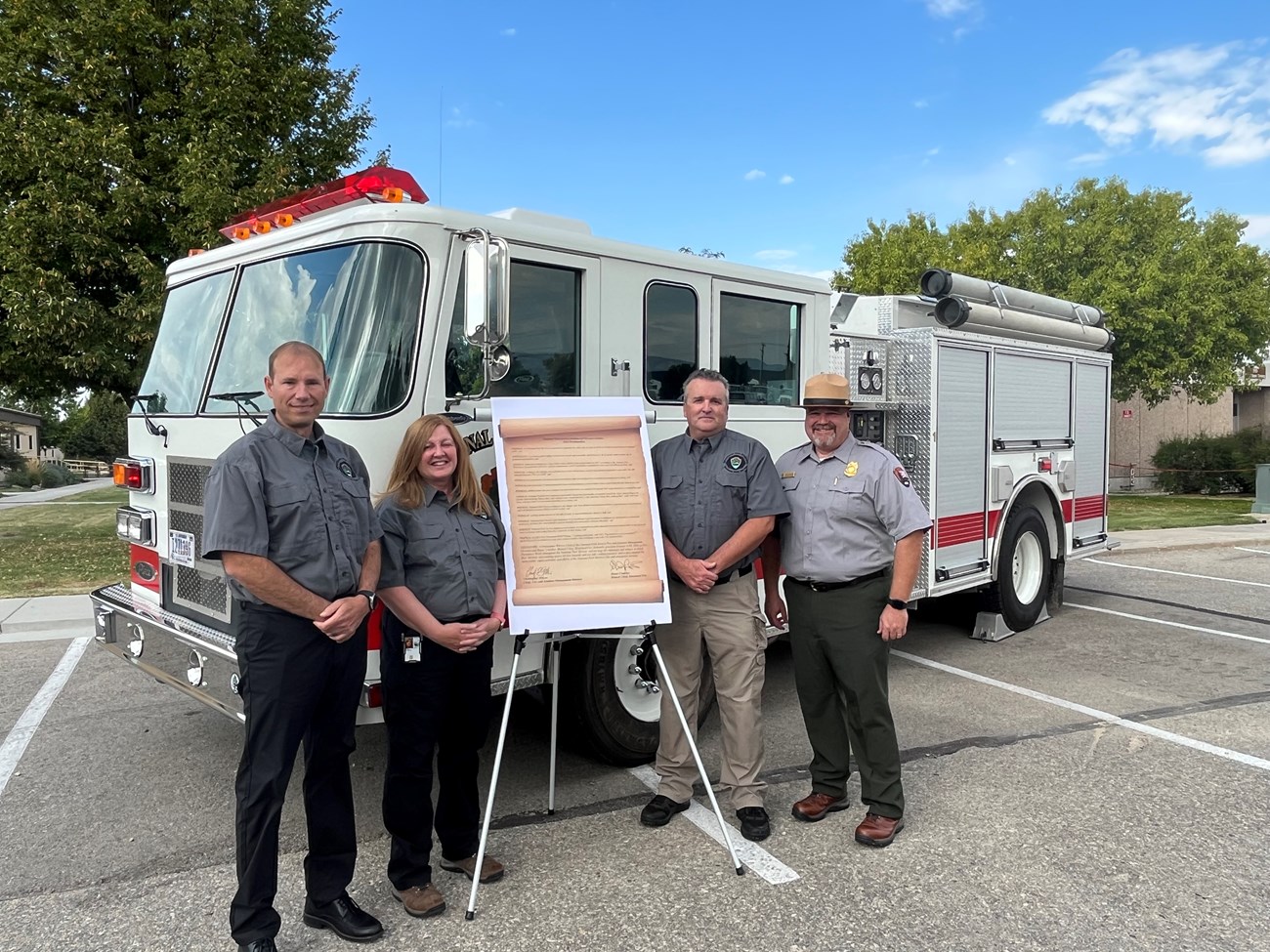 4 people stand in front of a fire engine with an easel displaying fire proclamation week text