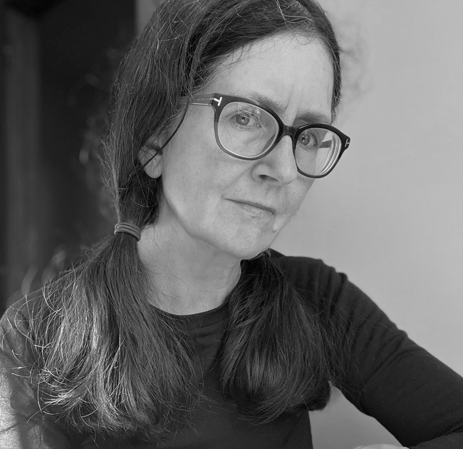 B&W photograph of a woman with long hair in loose pony tails and large glasses with dark frames