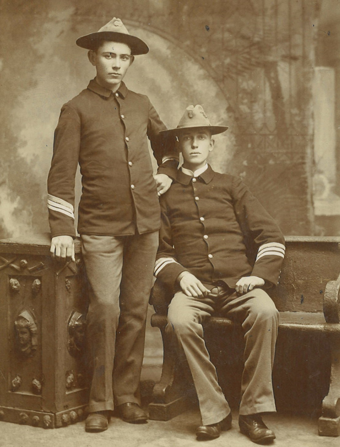 A black and white image of two men in a portrait studio wearing military uniforms. Christopher Ambrose Dunnigan is a young man with dark hair.