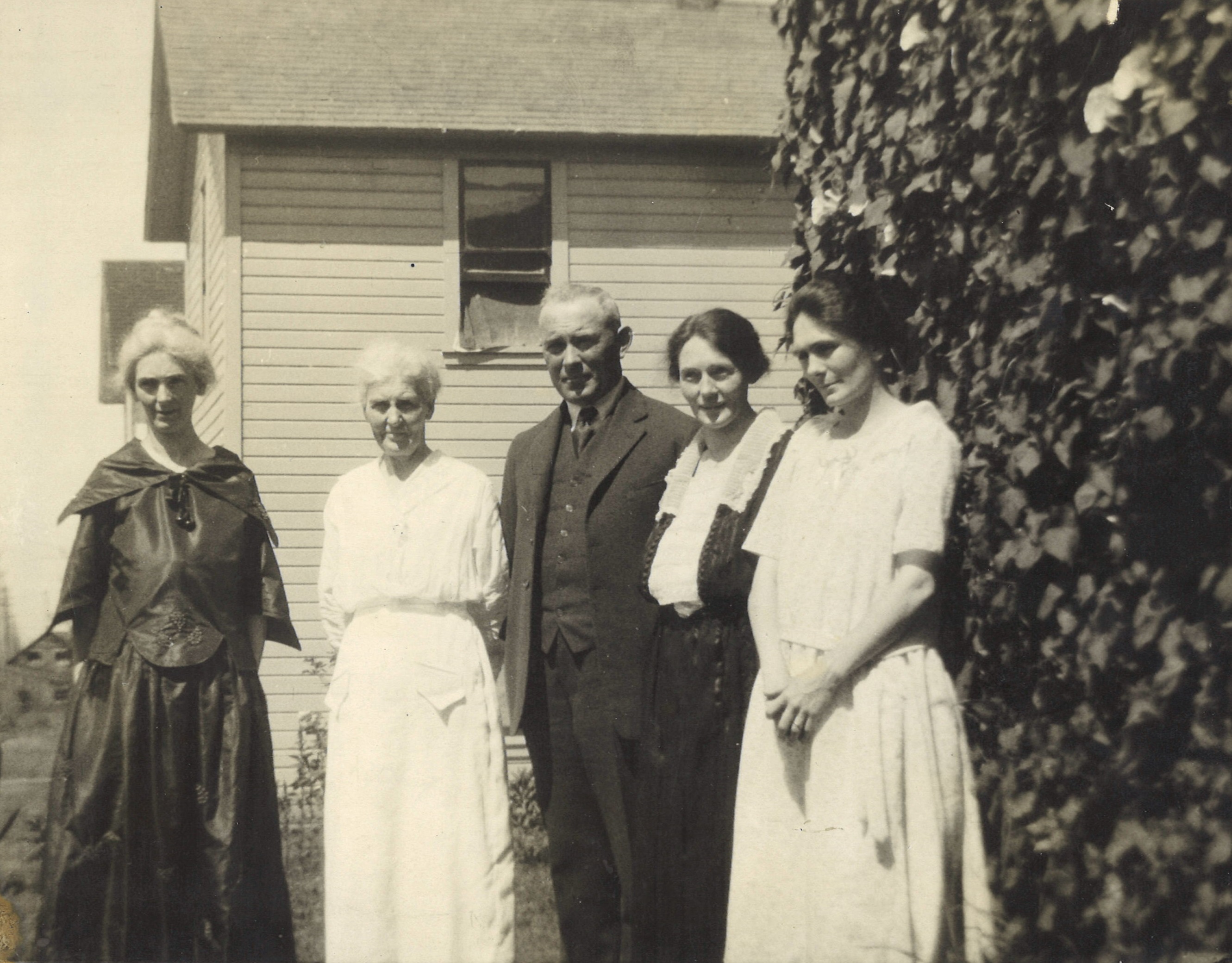 A black and white photo of four women wearing dresses and a man wearing a suit.
