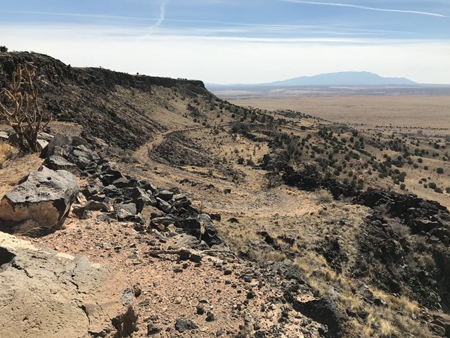 An old dirt road snakes down a large sandy cliff face in the desert.