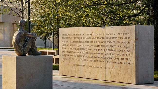 Bronze statue of Eisenhower seated as a boy from back facing large stone slap engraved with quote