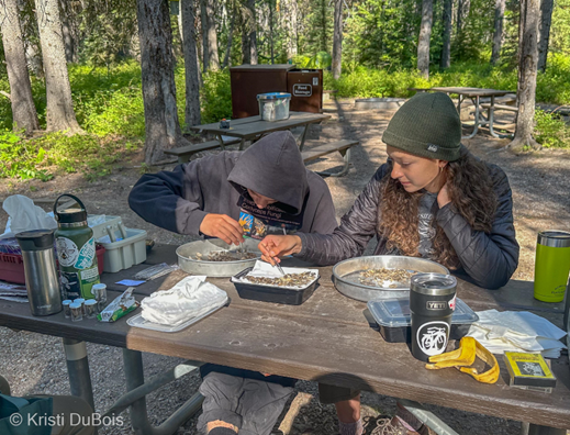 Two people sit at a picnic table and use tweezers to sort moths into a metal pan.