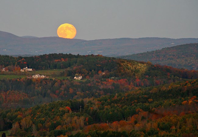 a full moon rises over rolling hills painted in fall colors
