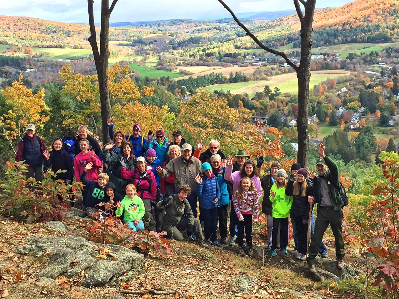 a group of people of varying ages gather with park ranger guides on a rolling hill view in the fall