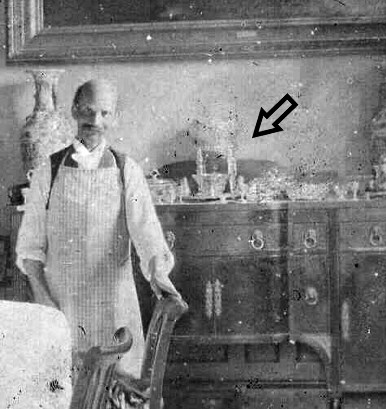 A historic black and white photograph of a waiter standing in the dining room with the Epergne on a shelf behind him.