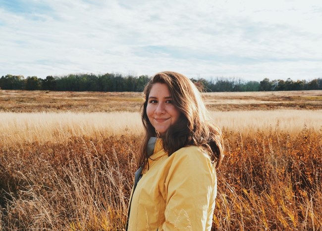 headshot of Evelyn wearing a yellow jacket and surrounded by a field of savanna in the background