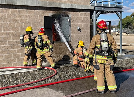 Firefighters spray water into an open window in a brick building to douse flames.