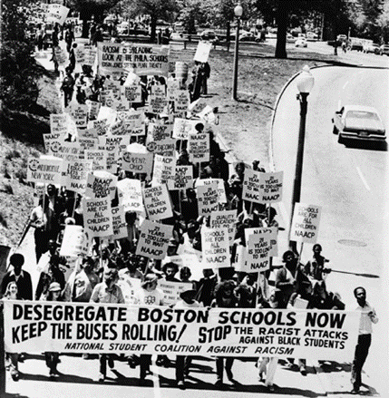 A crowd of people marching down a street with signs and banners promoting desegregation of busing