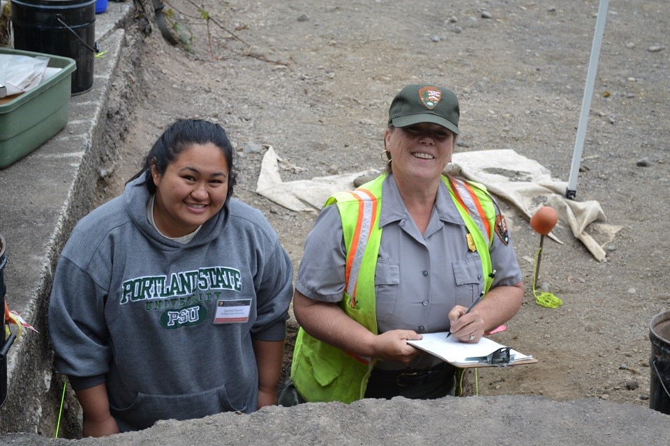 A woman wearing a Portland State University stands next to a woman wearing a National Park Service uniform holding a clipboard. They both are smiling at the camera.