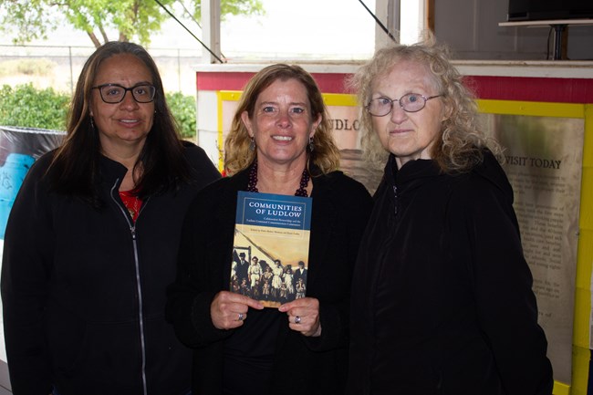 Three women; center woman holds a book cover