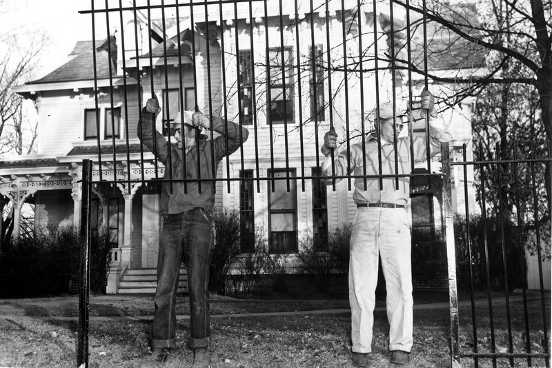 Two men installing black iron fence