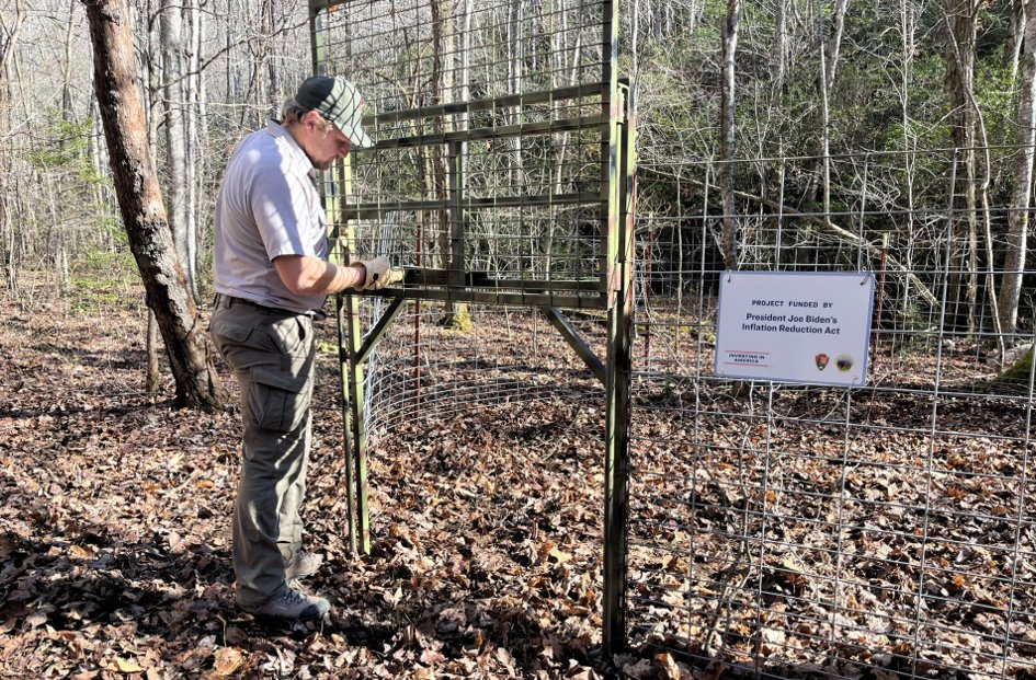 A uniformed individual stands in front of a metal enclosure, with a sign hanging on it