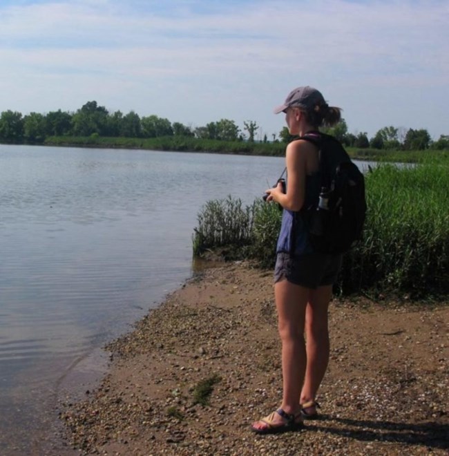 a woman standing on a river bank looking at into the water