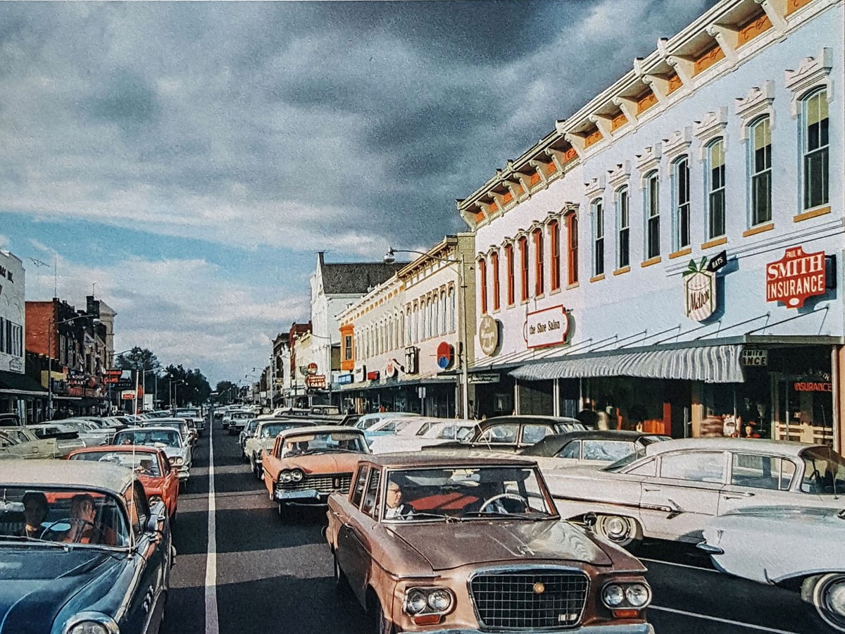 Looking down bumper to bumper traffic on a city street with brick building store fronts and angle parking.