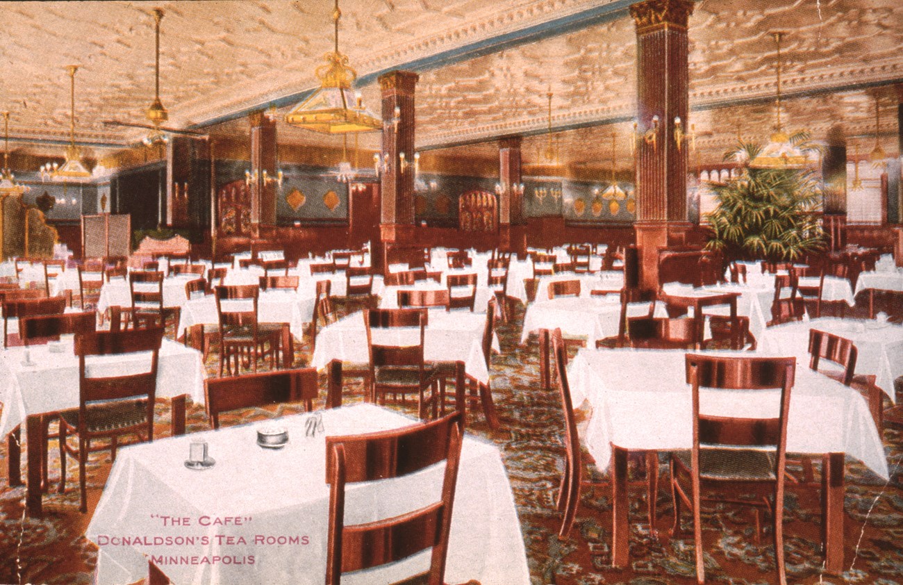 A large room filled with over 30 tables with white tablecloths and four chairs.