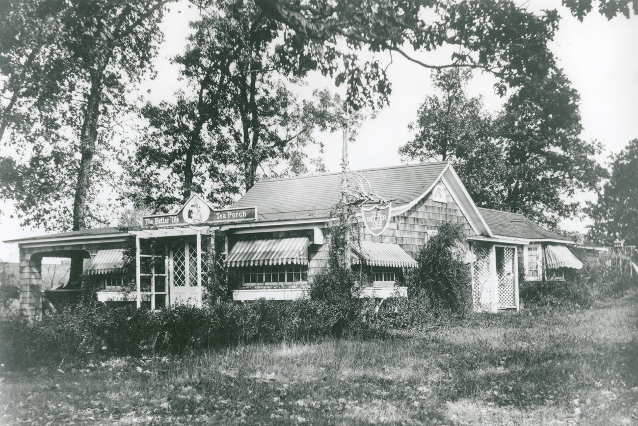 A house like building surrounded by shrubs and grass sign reads the better ‘ole tea porch.