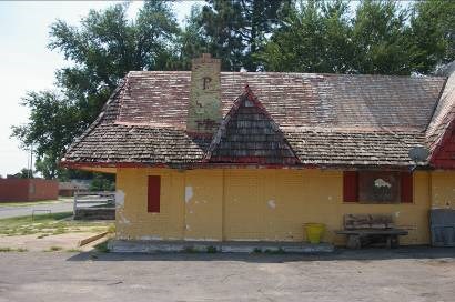 Yellow brick building with a mismatched roof with extended eves and overhangs.